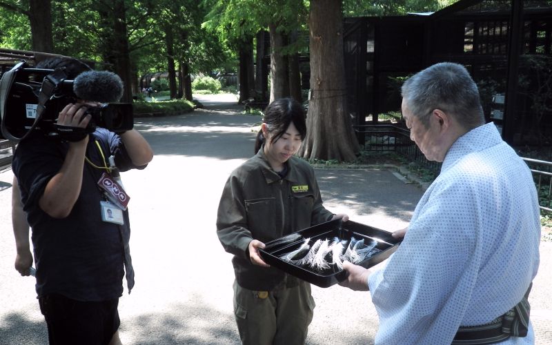 NHKのカメラの前で羽根を譲渡する東條裕子さんと東川光夫さん